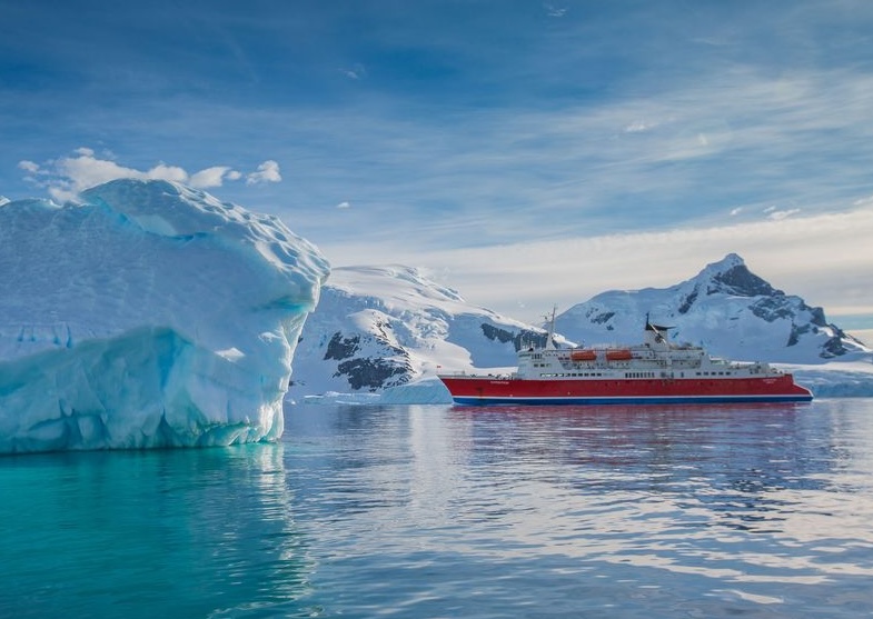 G Adventures expedition ship in Antarctic waters with large iceberg